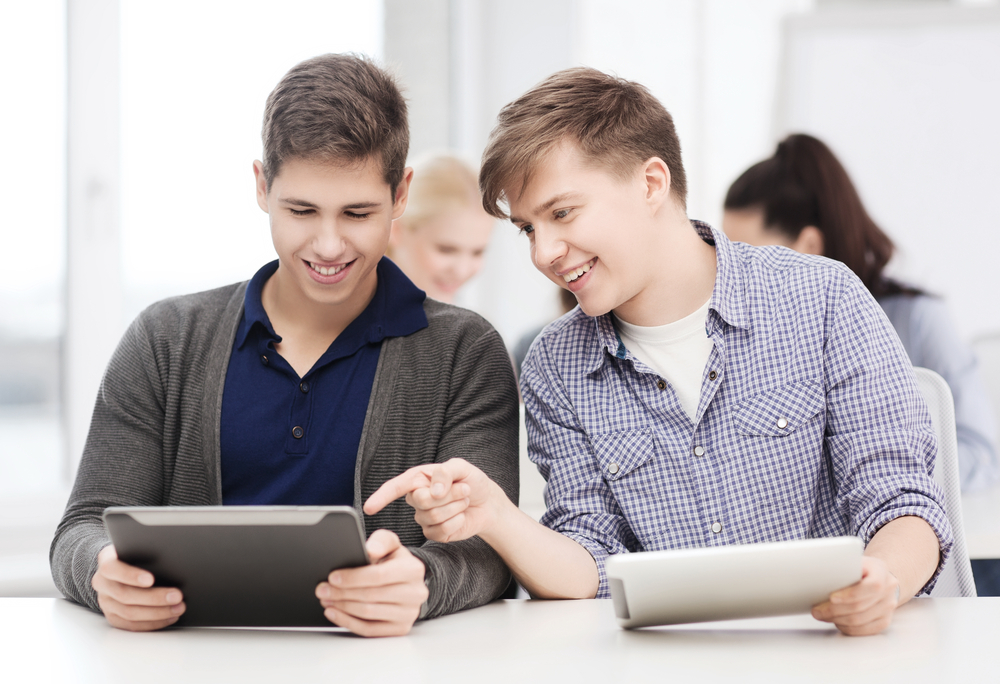 Dois jovens segurando tablets, fazendo uso da tecnologia na educação e conversando.